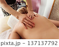 Close-up of professional massage therapist hands applying pressure on a woman bare back in calm spa room with warm natural light, soft tones, and relaxing atmosphere 137137792