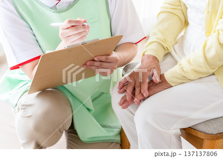 問診票に記入するスタッフと高齢者の手元 問診票に記入するスタッフと高齢者の手元 137137806