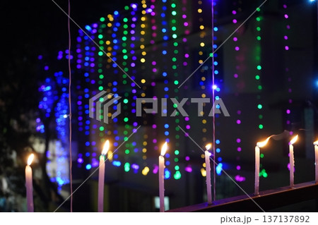 Burning candles on railing with colorful bokeh festive lights background Burning candles on railing with colorful bokeh festive lights background 137137892