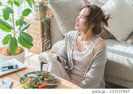 リビングテーブルで食事をするおしゃれな若いアジア人女性 リビングテーブルで食事をするおしゃれな若いアジア人女性 137137947