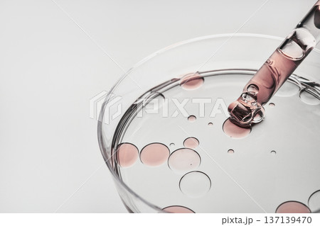 Dropper releasing cosmetic liquid and oil bubbles into clear dish on white background Dropper releasing cosmetic liquid and oil bubbles into clear dish on white background 137139470