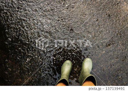 POV shot of person with rain boots standing on wet ground during rainfall, with raindrops in Rainy season 137139491
