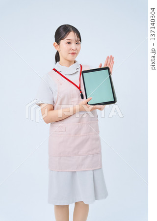 白衣とエプロンを着てデジタル機器を持つ若い女性 白衣とエプロンを着てデジタル機器を持つ若い女性 137140304
