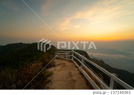 Adventurous traveler standing on a mountain peak viewpoint enjoying a spectacular sunrise and sea of clouds. Adventurous traveler standing on a mountain peak viewpoint enjoying a spectacular sunrise and sea of clouds. 137140363