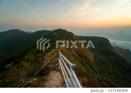 Adventurous traveler standing on a mountain peak viewpoint enjoying a spectacular sunrise and sea of clouds. Adventurous traveler standing on a mountain peak viewpoint enjoying a spectacular sunrise and sea of clouds. 137140364