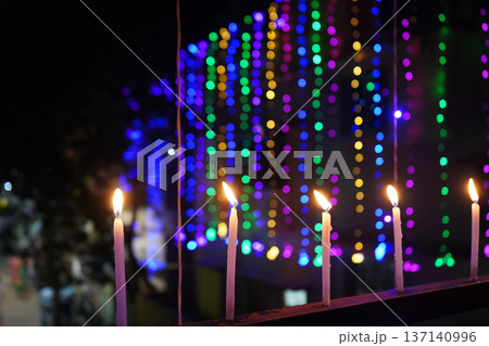 Row of lit candles on balcony railing against vibrant multicolored bokeh background Row of lit candles on balcony railing against vibrant multicolored bokeh background 137140996