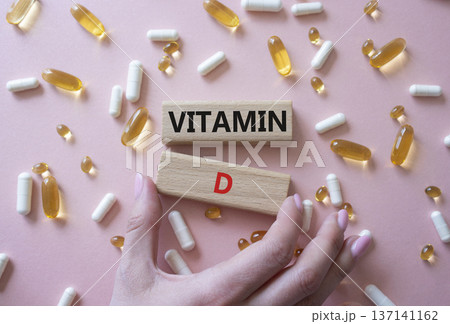 Vitamin D symbol. Concept word Vitamin D on wooden blocks. Beautiful pink background with pills. Doctor hand. Medicine and Vitamin D concept. Copy space Vitamin D symbol. Concept word Vitamin D on wooden blocks. Beautiful pink background with pills. Doctor hand. Medicine and Vitamin D concept. Copy space 137141162