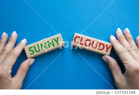 Sunny or Cloudy symbol. Concept word Sunny or Cloudy on wooden blocks. Businessman hand. Beautiful blue background. Business and Sunny or Cloudy concept. Copy space 137141166