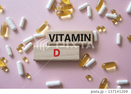 Vitamin D symbol. Concept word Vitamin D on wooden blocks. Beautiful pink background with pills. Medicine and Vitamin D concept. Copy space Vitamin D symbol. Concept word Vitamin D on wooden blocks. Beautiful pink background with pills. Medicine and Vitamin D concept. Copy space 137141209