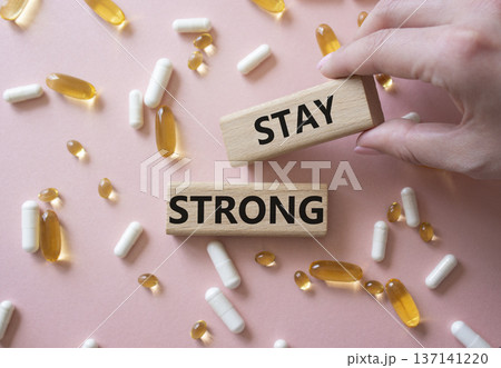 Stay Strong symbol. Concept word Stay Strong on wooden blocks. Beautiful pink background with pills. Doctor Hand. Medicine and Stay Strong concept. Copy space Stay Strong symbol. Concept word Stay Strong on wooden blocks. Beautiful pink background with pills. Doctor Hand. Medicine and Stay Strong concept. Copy space 137141220
