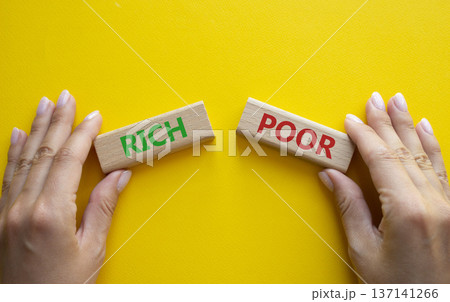 Rich vs Poor symbol. Concept word Rich vs Poor on wooden blocks. Businessman hand. Beautiful yellow background. Business and Rich vs Poor concept. Copy space Rich vs Poor symbol. Concept word Rich vs Poor on wooden blocks. Businessman hand. Beautiful yellow background. Business and Rich vs Poor concept. Copy space 137141266