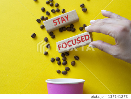 Stay Focused symbol. Concept word Stay Focused on wooden blocks. Beautiful yellow background with coffee cup. Businessman hand. Business and Stay Focused concept. Copy space 137141278