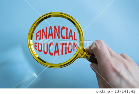 Financial Education symbol. Magnifying Glass with Concept word Financial Education. Businessman hand. Beautiful blue background. Business and Financial Education concept. Copy space 137141342