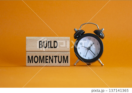Build momentum symbol. Wooden blocks with words Build momentum. Beautiful orange background with alarm clock. Business and Build momentum concept. Copy space. 137141365