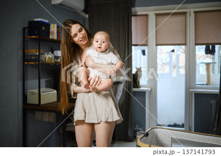 Mother holds baby in apartment with sunlight shining through windows 137141793