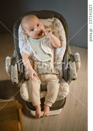 Baby sitting in a high chair enjoying a snack in a quiet room 137141825