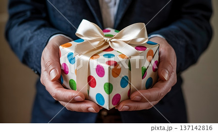 Elegantly Wrapped Colorful Polka Dot Gift Box Held in Well-Manicured Hands 137142816