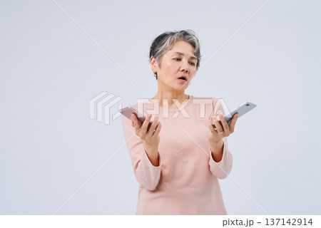 2つのスマートフォンを手に悩むシニア女性 2つのスマートフォンを手に悩むシニア女性 137142914