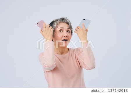 2つのスマートフォンを手に悩むシニア女性 2つのスマートフォンを手に悩むシニア女性 137142918