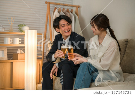 夜,帰宅後にソファに座りながらビールを飲む若いアジア人夫婦,カップル 137145725