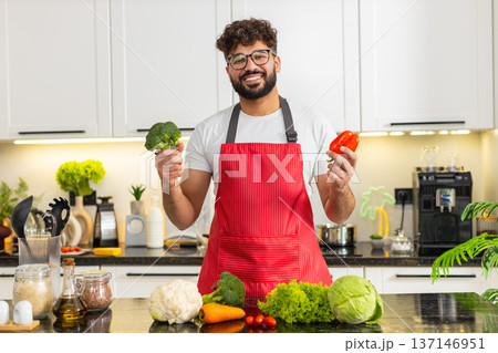 Arabian young adult man smiling with broccoli and red pepper in kitchen for healthy food meal prep Arabian young adult man smiling with broccoli and red pepper in kitchen for healthy food meal prep 137146951