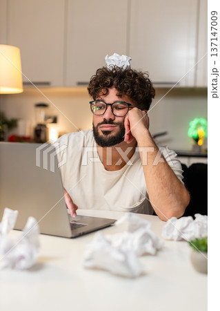 Arabian man fights creative block writes ideas for project crumpled papers desk frustrated evening Arabian man fights creative block writes ideas for project crumpled papers desk frustrated evening 137147009