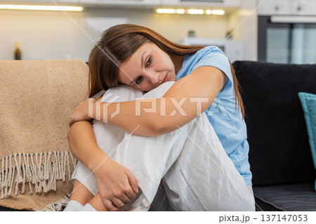 Young woman sits hugging knees sad after bad news stressed upset low mood anxious and lonely relief Young woman sits hugging knees sad after bad news stressed upset low mood anxious and lonely relief 137147053