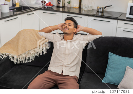 Indian man sits down to relax after long day takes slow breath closes eyes lets body and mind rest Indian man sits down to relax after long day takes slow breath closes eyes lets body and mind rest 137147081