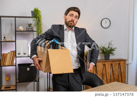 Middle-aged businessman packs personal items in box looks around room with gentle nostalgia softly 137147378