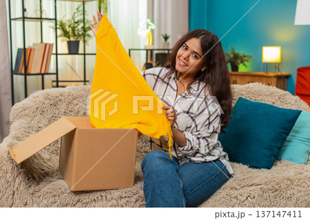 Indian woman unboxes delivery box finds new scarf smiles joy celebrating successful online shopping 137147411
