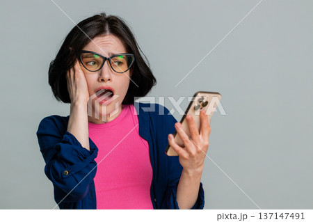 Woman looking at smartphone screen frowning sadly reacting to loss defeat or bad disappointing news Woman looking at smartphone screen frowning sadly reacting to loss defeat or bad disappointing news 137147491