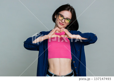 Woman making heart shape with fingers looking gently at camera expressing love affection caring Woman making heart shape with fingers looking gently at camera expressing love affection caring 137147493