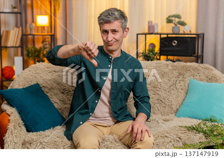Young man shows thumbs down gesture with serious expression showing disapproval or disagreement Young man shows thumbs down gesture with serious expression showing disapproval or disagreement 137147919