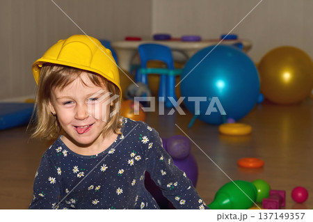 Laughing cheerful girl in protective helmet.Playroom in kindergarten Laughing cheerful girl in protective helmet.Playroom in kindergarten 137149357
