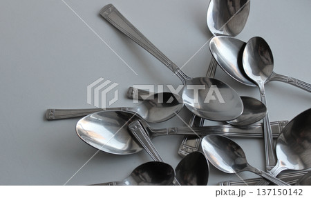 Big And Small Metallic Spoons Scattered On White At A Side Of Image With Clean Part For Title Or Logo. Dishware Concept Design Stock Photo 137150142