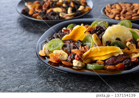 Dried tropical fruits, nuts, and raisins in black plate. Dried tropical fruits, nuts, and raisins in black plate. 137154139
