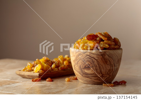 Yellow sultana raisins in a wooden bowl on a beige background. 137154145