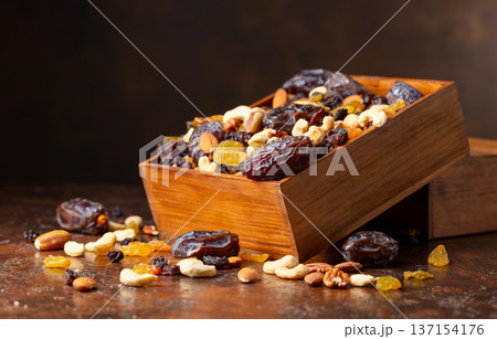 Dates, nuts, and raisins in a wooden box on a brown background. Dates, nuts, and raisins in a wooden box on a brown background. 137154176