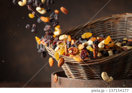 Mix of various nuts and raisins in a old basket on a brown background. 137154177