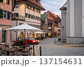 Wangen stadtmitte, germany, august 17, 2023. Cobblestone street and colorful historic buildings in meersburg, southern germany, featuring an outdoor cafe and a approaching red car 137154631