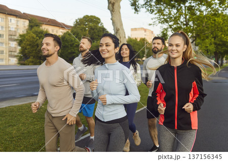Group of runners jogging marathon in summer city park, team running along road Group of runners jogging marathon in summer city park, team running along road 137156345