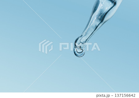 Dropper dispensing single clear liquid drop against blue background, symbolizing hydration Dropper dispensing single clear liquid drop against blue background, symbolizing hydration 137156642