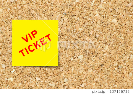 Yellow note paper with word VIP ticket on cork board background with copy space 137156735