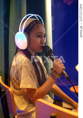 A girl in luminous headphones speaks into a microphone while giving an interview on a radio broadcast. Children's Vocal School 137157264