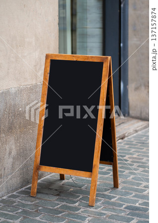 Blank wooden chalkboard a-frame sign standing on a cobbled sidewalk, offering a clear space for custom text or graphics, ideal for advertising and marketing messages Blank wooden chalkboard a-frame sign standing on a cobbled sidewalk, offering a clear space for custom text or graphics, ideal for advertising and marketing messages 137157874