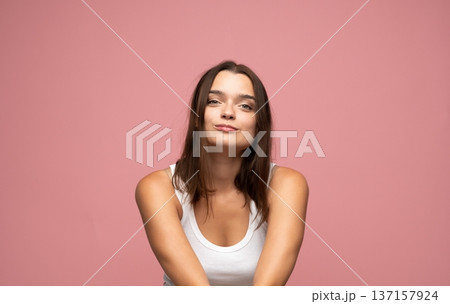 Young woman showing confident smirk, looking at camera with playful facial expression on pink background Young woman showing confident smirk, looking at camera with playful facial expression on pink background 137157924