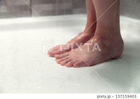 Close-up of Female bare feet standing on wet shower floor with water droplets, tiles visible in the background, creating a clean and refreshing bathroom atmosphere Close-up of Female bare feet standing on wet shower floor with water droplets, tiles visible in the background, creating a clean and refreshing bathroom atmosphere 137159403