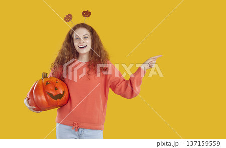 Happy funny woman holding Halloween pumpkin, advertising sale, pointing away and smiling 137159559