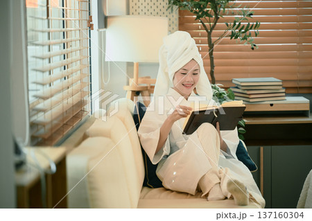 Young woman in bathrobe reads book on sofa 137160304