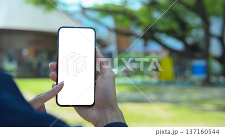 Hands holding smartphone with blank screen inside a modern community mall Hands holding smartphone with blank screen inside a modern community mall 137160544